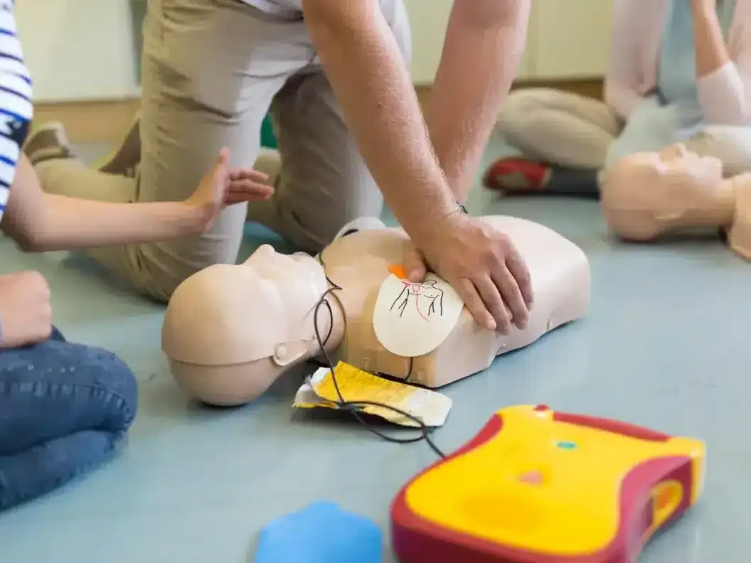 Trainees practising CPR on mannequins beside a training defibrillator during a first aid course