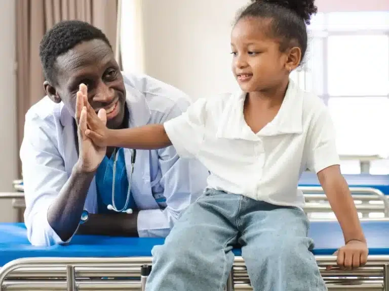 Doctor giving a smiling young patient a high five on a hospital bed