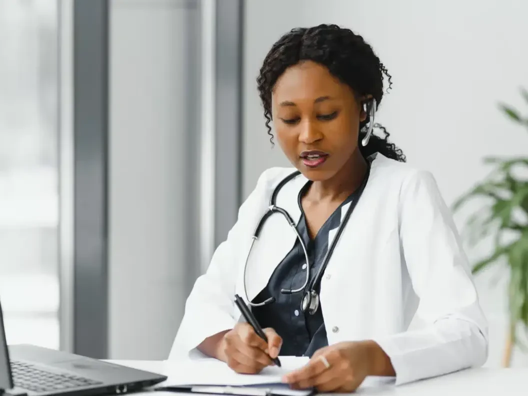 Doctor writing patient notes at her desk during a video consultation