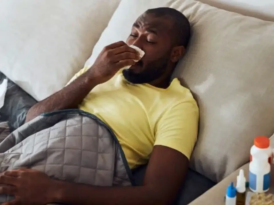 Man resting in bed with a cold, with tissues on the table beside him