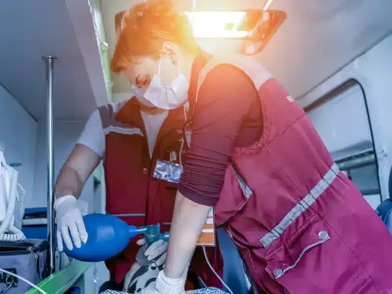 Paramedic in a red uniform treating a patient on a stretcher inside an ambulance