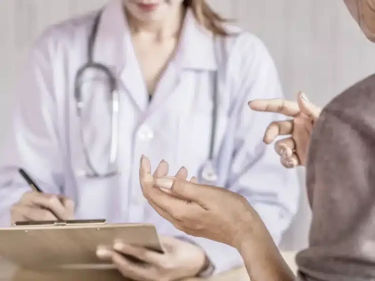 Patient explaining a health concern to a doctor who takes notes on a clipboard